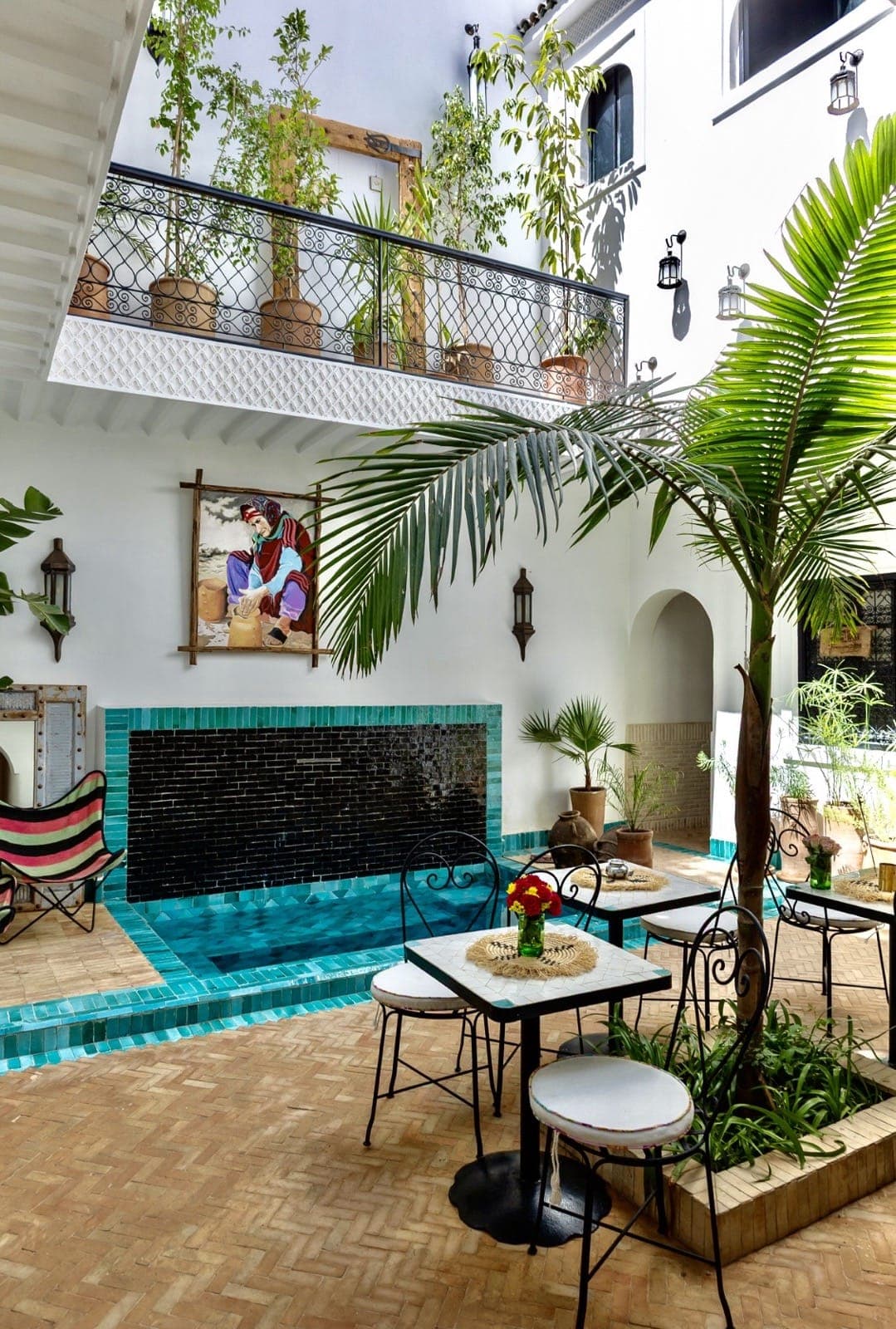 The courtyard of Riad Taww'Ami: a turquoise plunge pool under the balcony, lanterns and palms